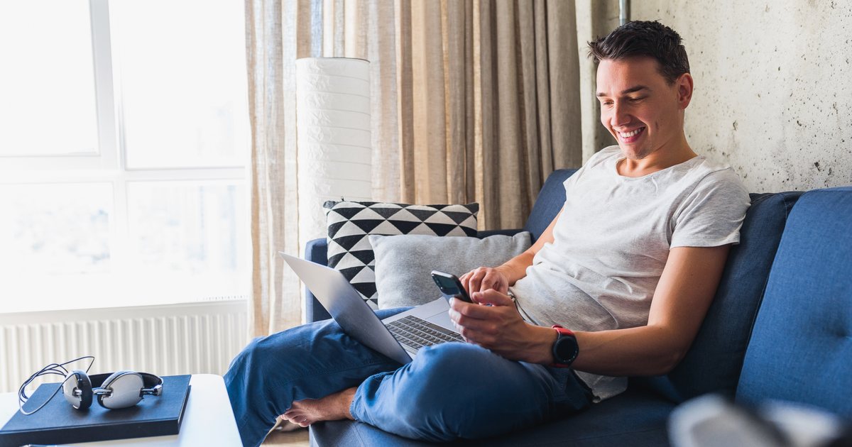 A man using a phone and laptop on a sofa