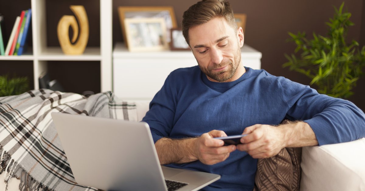 A man reviewing his phone beside a laptop at home