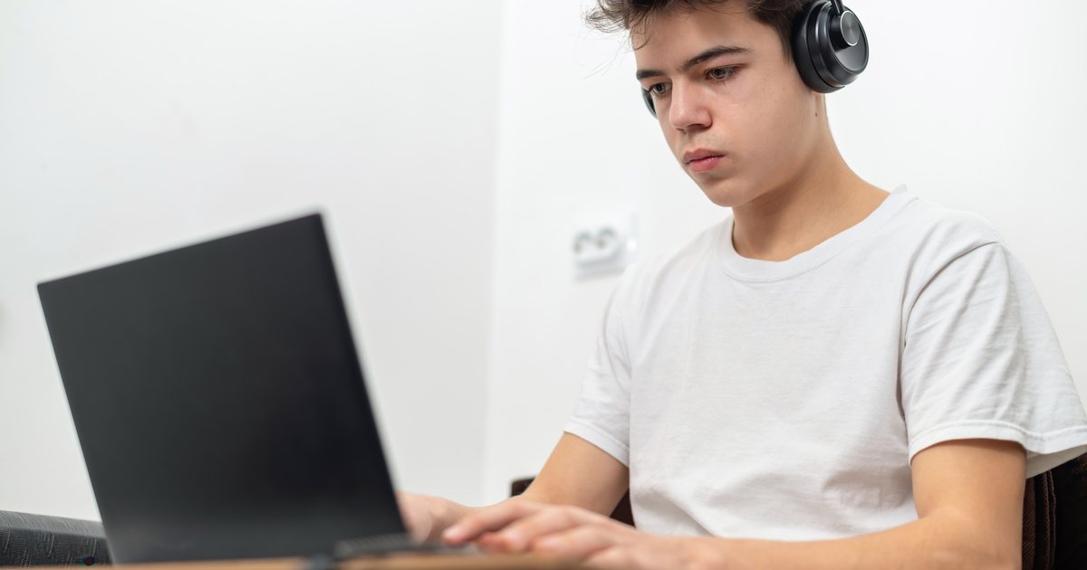 A teenage boy studying with a laptop and headphones