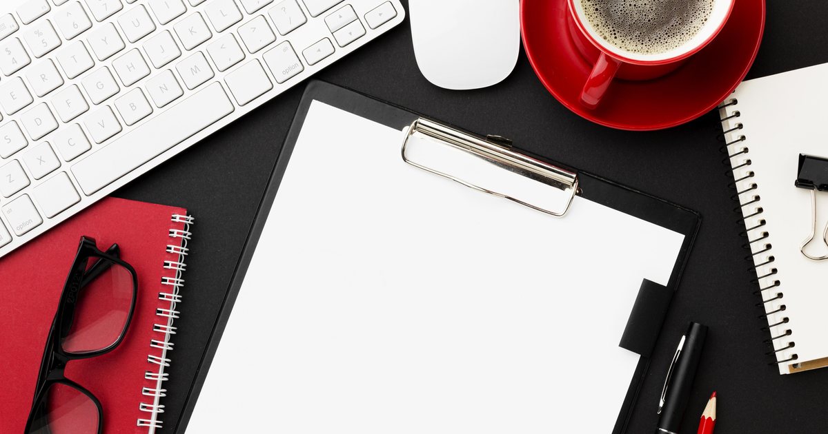 A clipboard with paper beside a notebook and keyboard