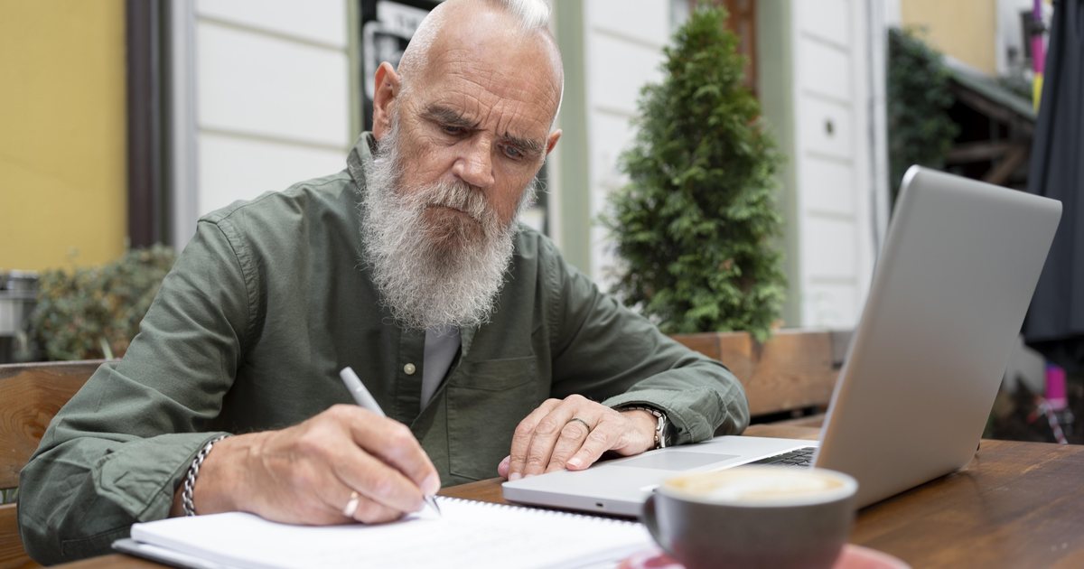 A man writing in a notebook while studying at a laptop