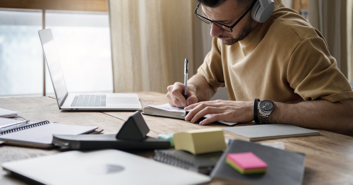 A man writing study notes beside a laptop