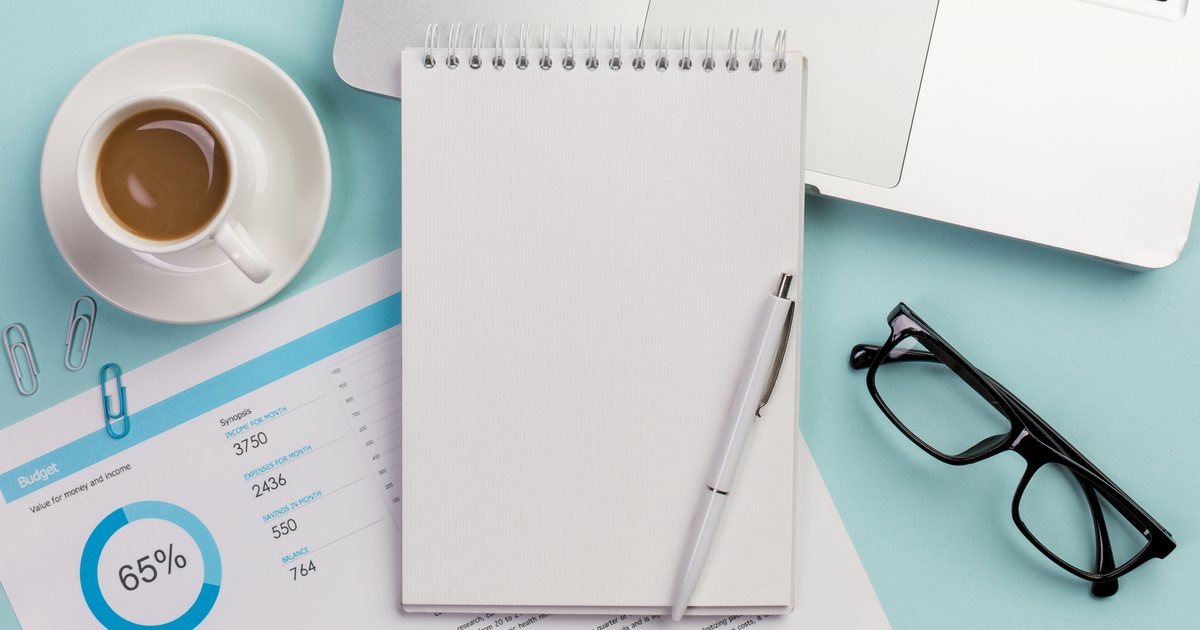 A budget worksheet, notebook and glasses on a blue desk