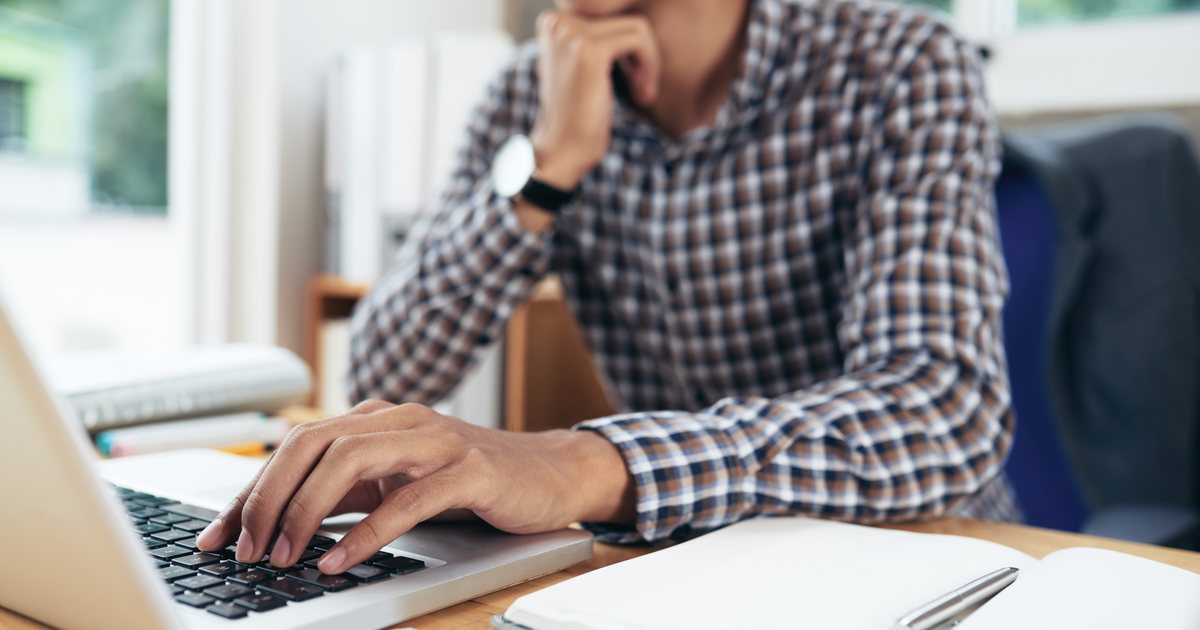 A man reviewing information beside a laptop and notebook