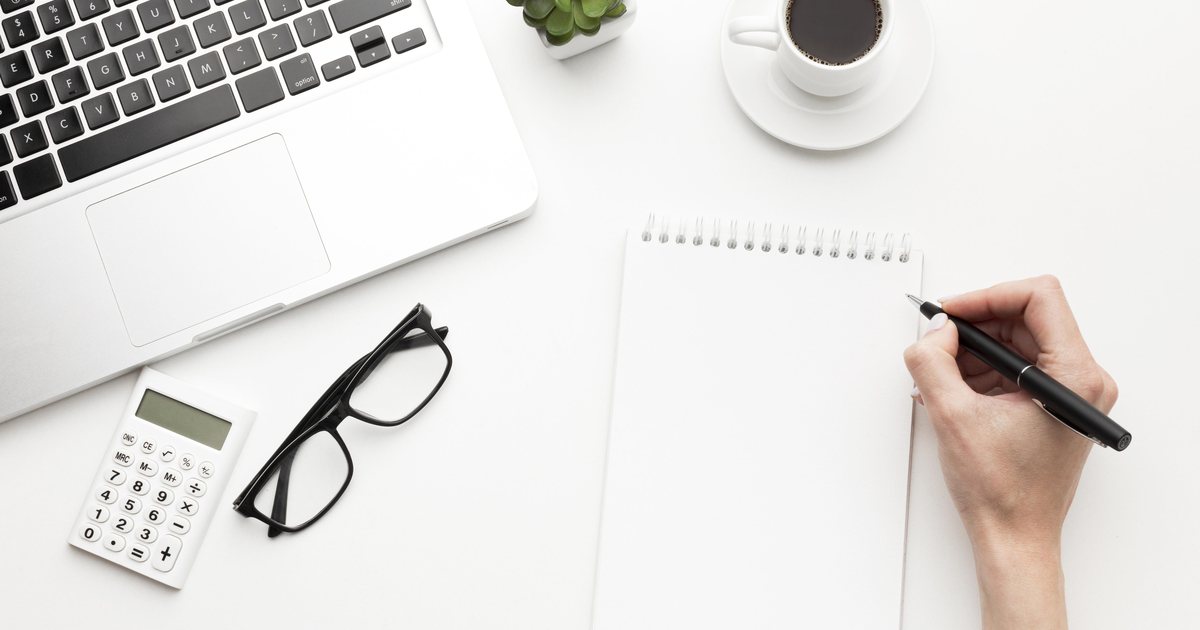 A hand writing notes beside a laptop