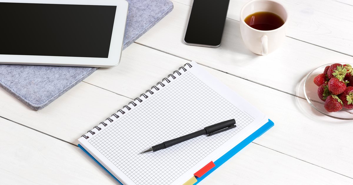 An open notebook, pen and tablet arranged on a desk