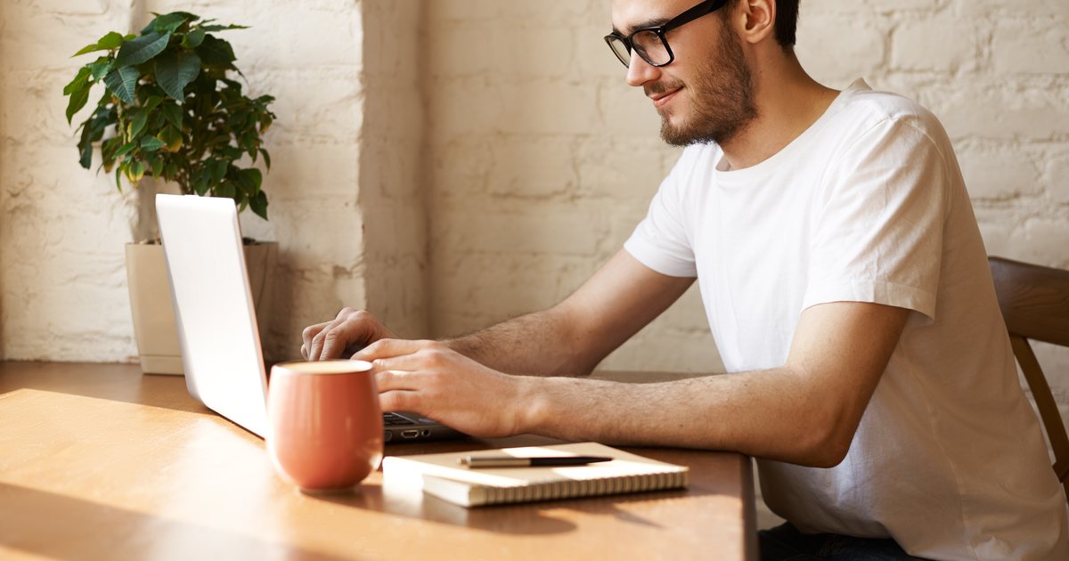 A man writing notes at a desk beside a window