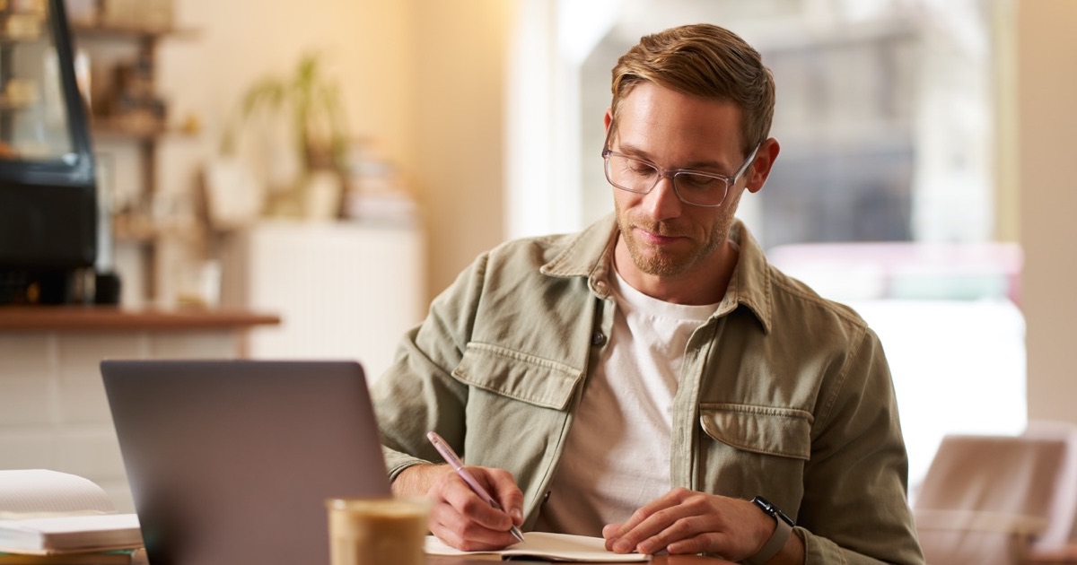 A man reviewing his notes beside a laptop